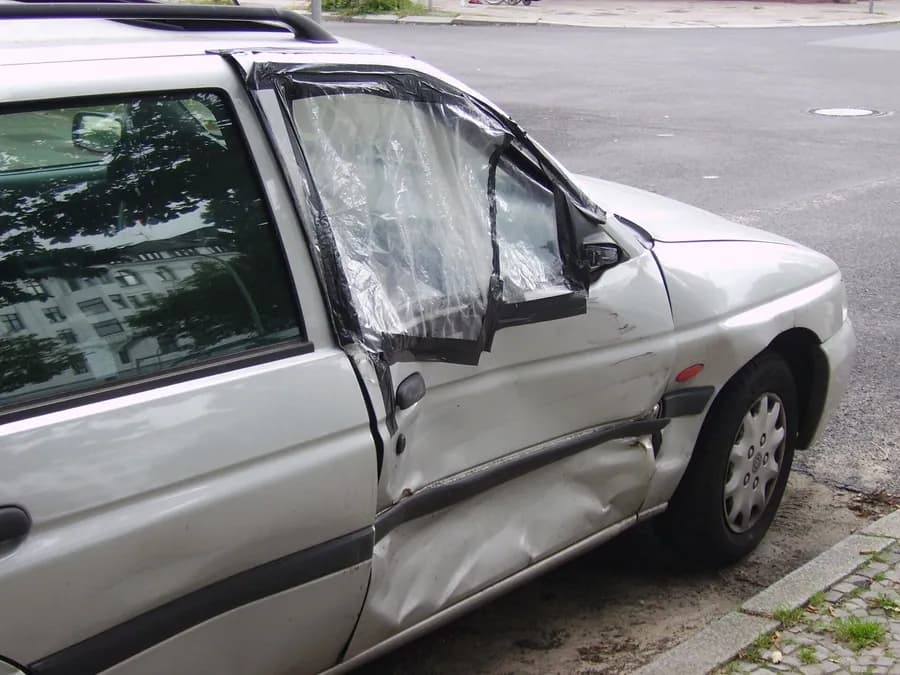 Yan kapısı çökmüş, camı kırılıp naylonla kapatılmış gümüş renkli station wagon otomobilin kaporta hasarı yakın çekimde